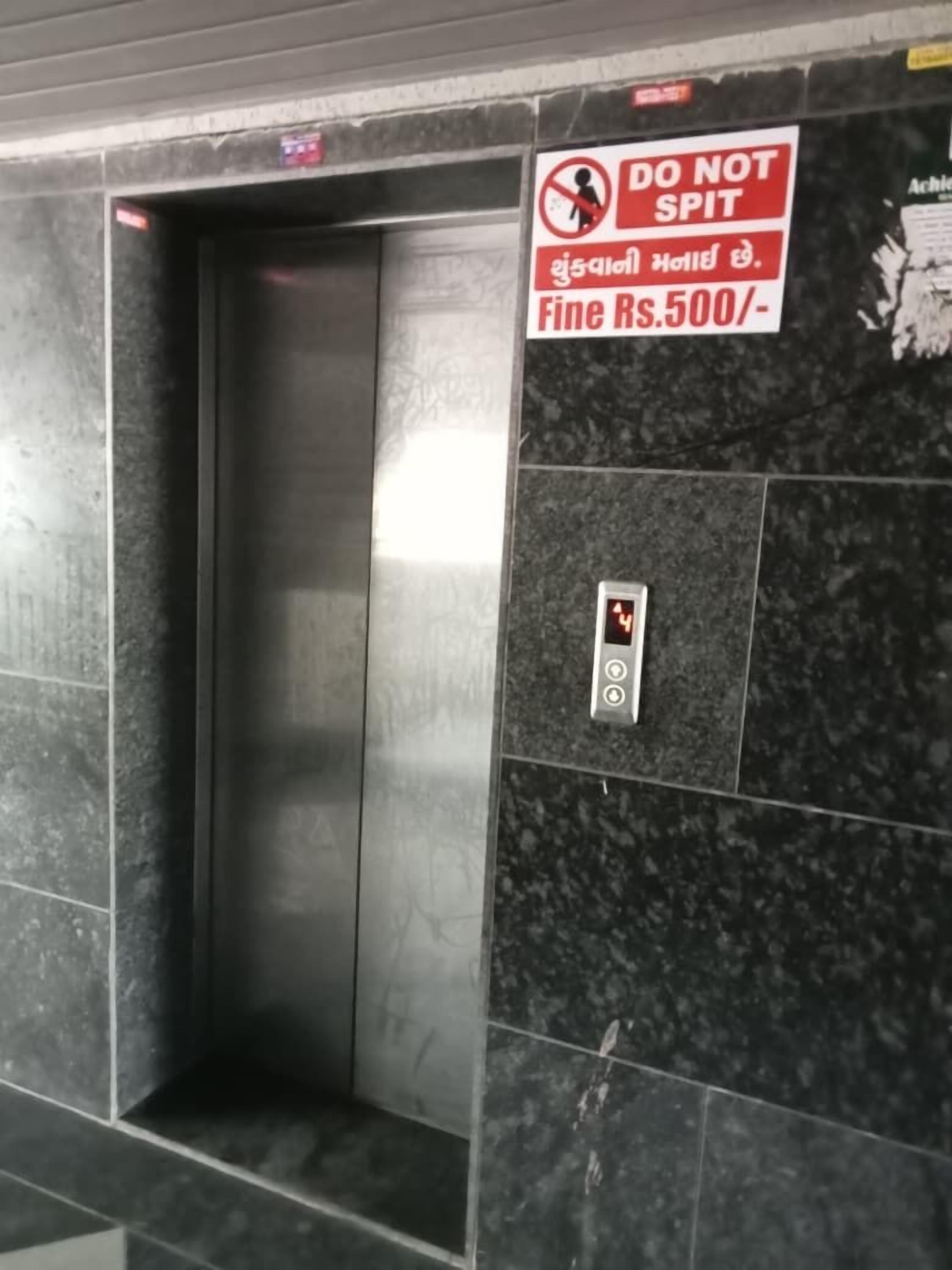 Un ascensore con un cartello che recita “NON SPUTARE” e una multa di 500 rupie per eventuali infrazioni.