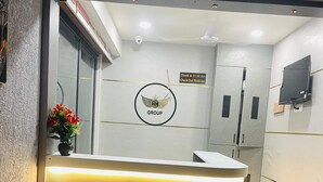 Ein Empfangsbereich mit einer Rezeption, einem an der Wand befestigten Schild mit Ein- und Auscheckzeiten, einer Überwachungskamera und einer Blumenvase.