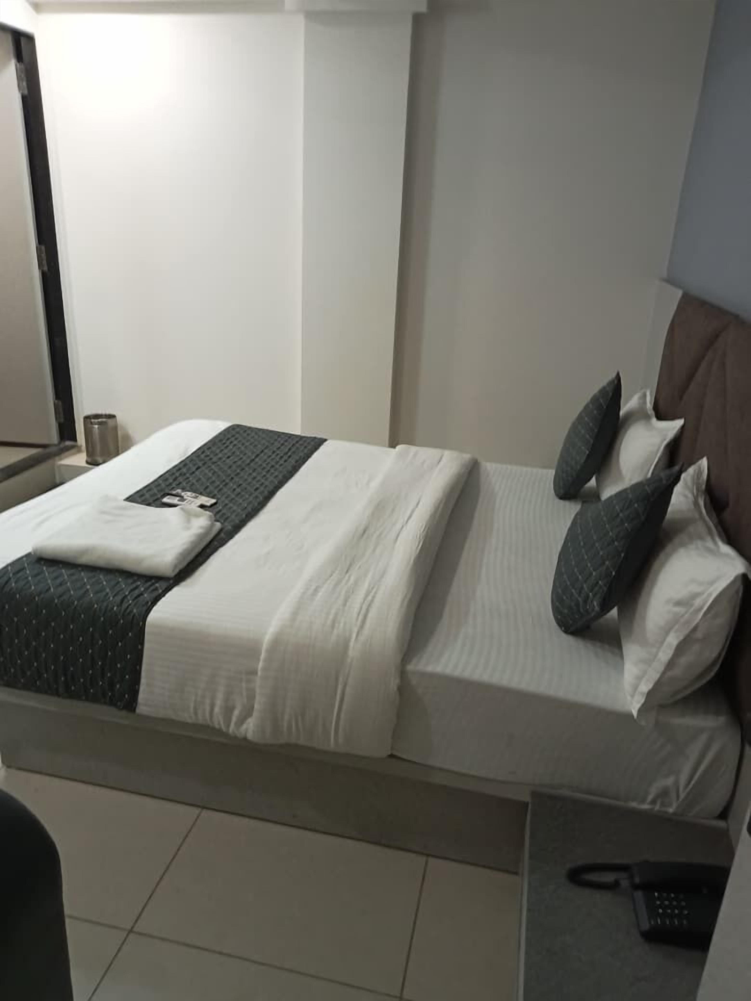 A neatly made bed with a white and gray duvet, two pillows, and a folded towel. A telephone is on a small table beside the bed.