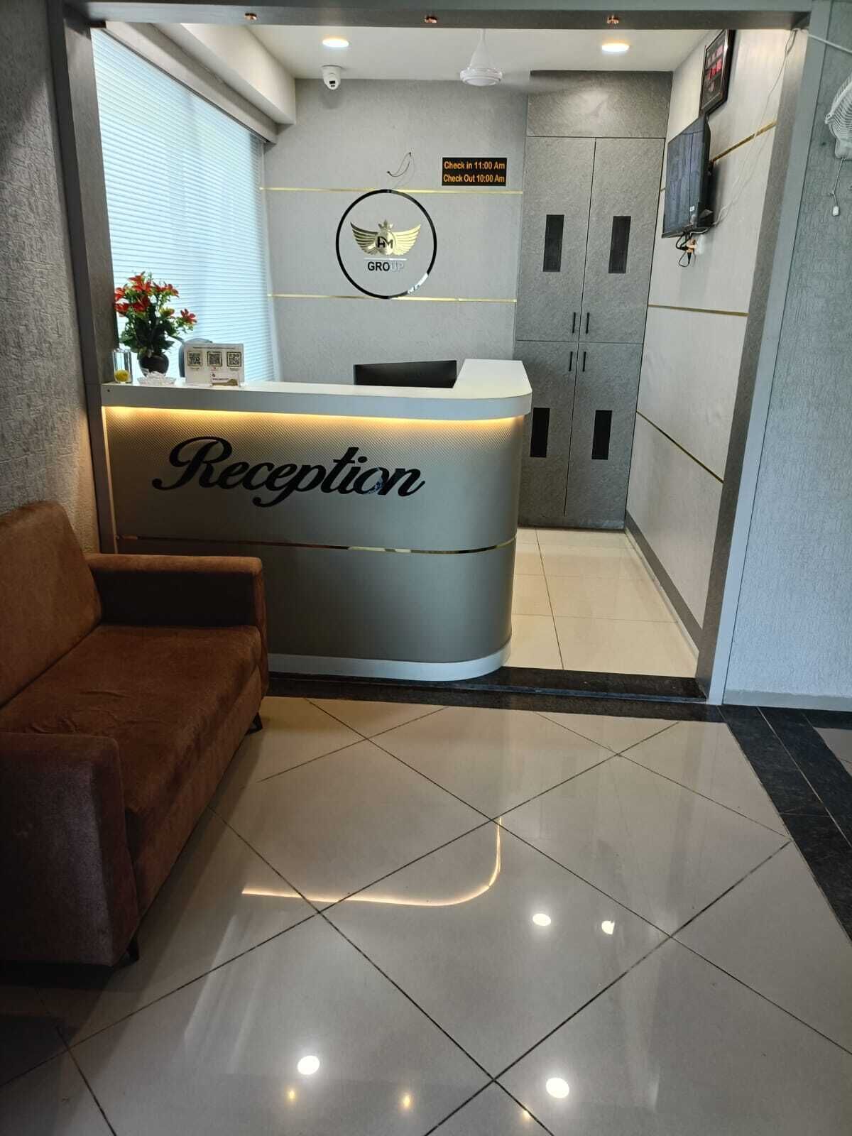 A reception area with a reception desk labeled "Reception," a sign indicating check-in and check-out times, a wall-mounted television, and a sofa.