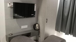 Ein modernes Zimmer mit grauem Sofa, einem Flachbildfernseher an der Wand, einem Wasserkocher und einem Schrank.