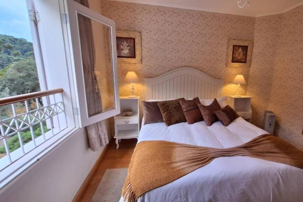 Ein Schlafzimmer mit einem großen Bett, zwei Nachttischen mit Lampen, einem Fenster mit Ausblick und einem Spiegel an der Wand.