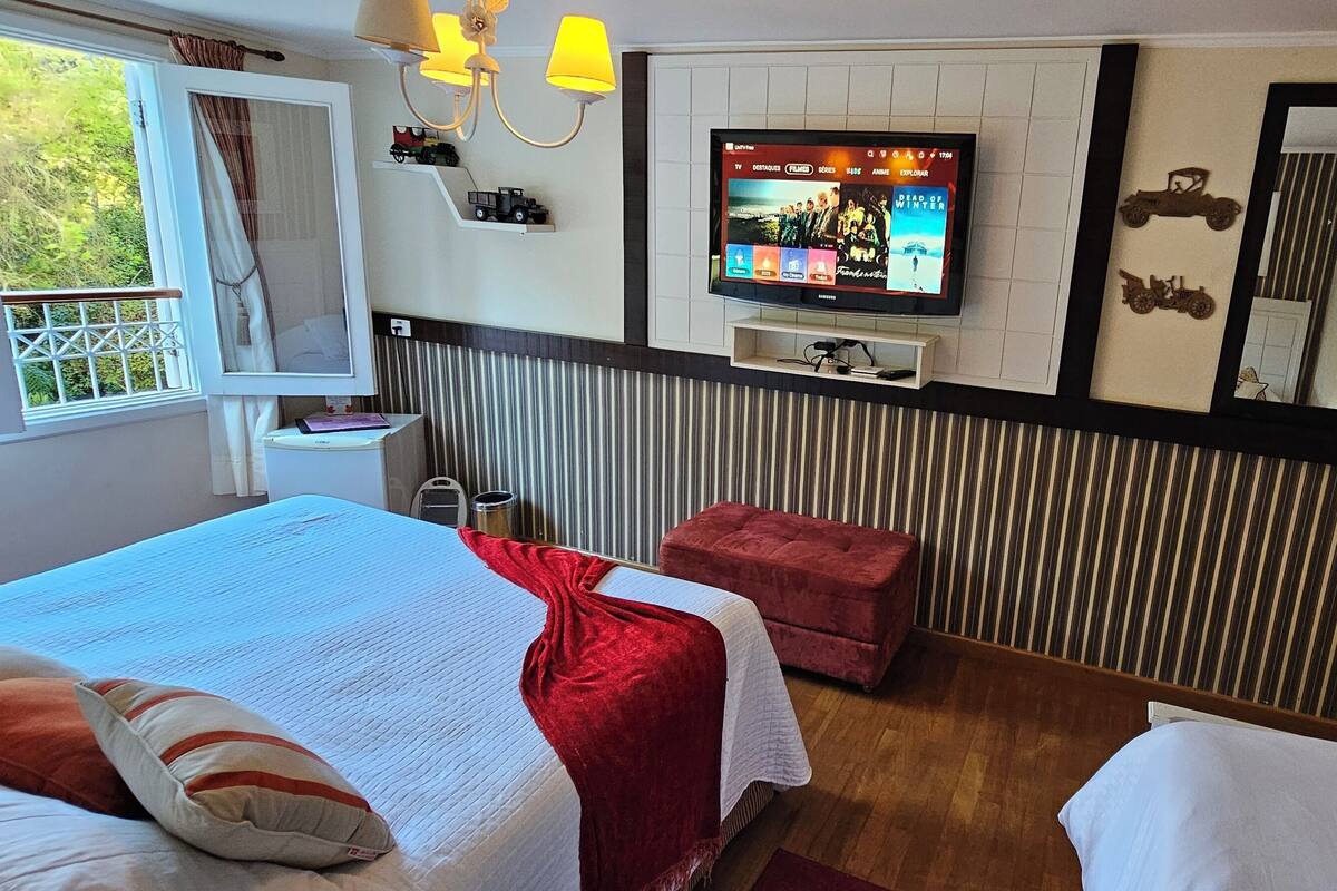 Ein Hotelzimmer mit zwei Betten, einem Fernseher, einem Fenster mit Vorhängen, einem Heizkörper und einem Spiegel mit Fahrzeugverzierungen.