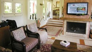 Uma sala de estar com lareira, televisão e escada que dá para outro cômodo.