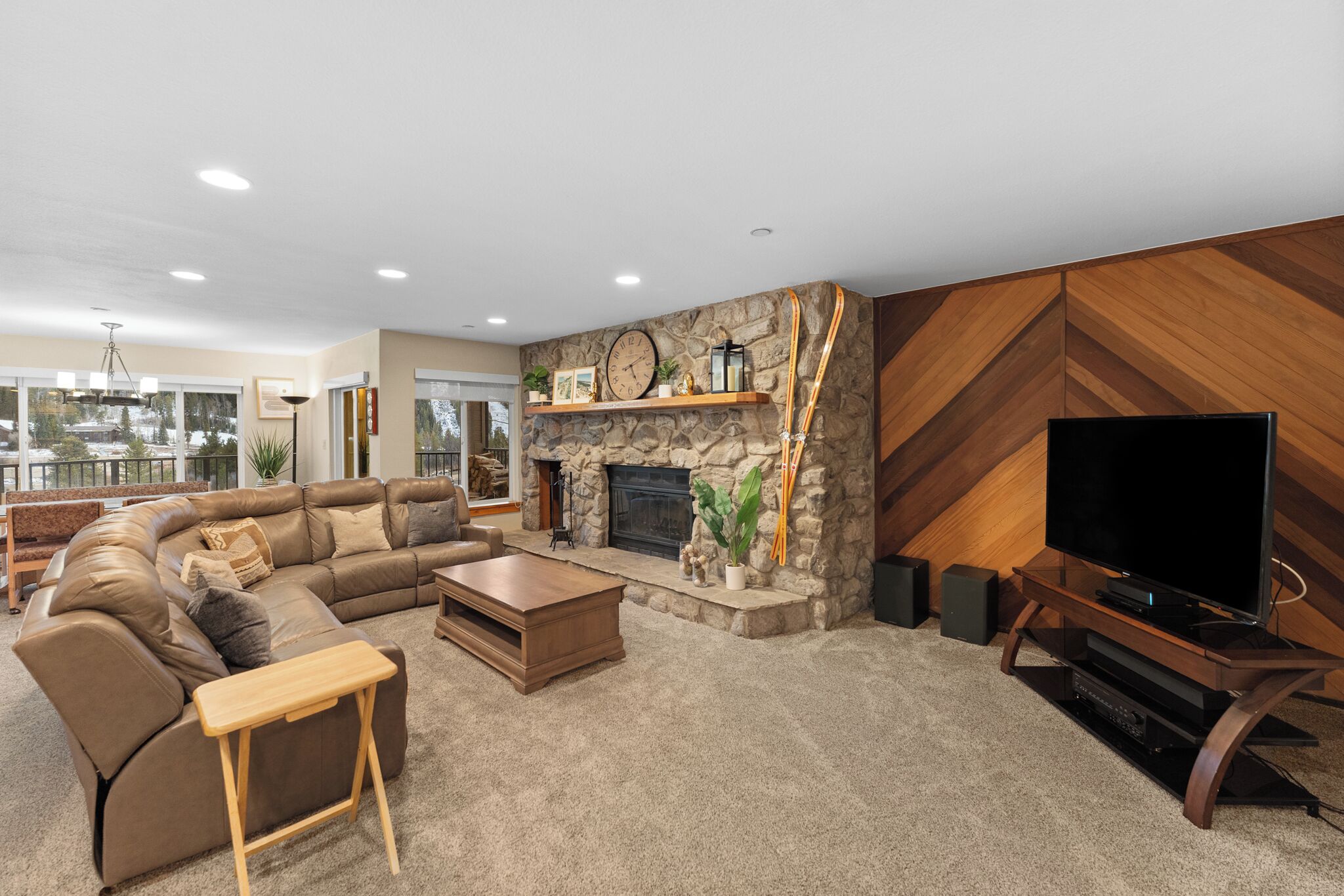 A modern living room with a stone fireplace, a large flat-screen TV, a sectional sofa, and a wooden coffee table.