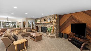 A modern living room with a stone fireplace, a large flat-screen TV, a sectional sofa, and a wooden coffee table.