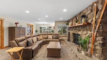 A spacious living room with a large L-shaped sectional sofa, a wooden coffee table, and a stone fireplace.