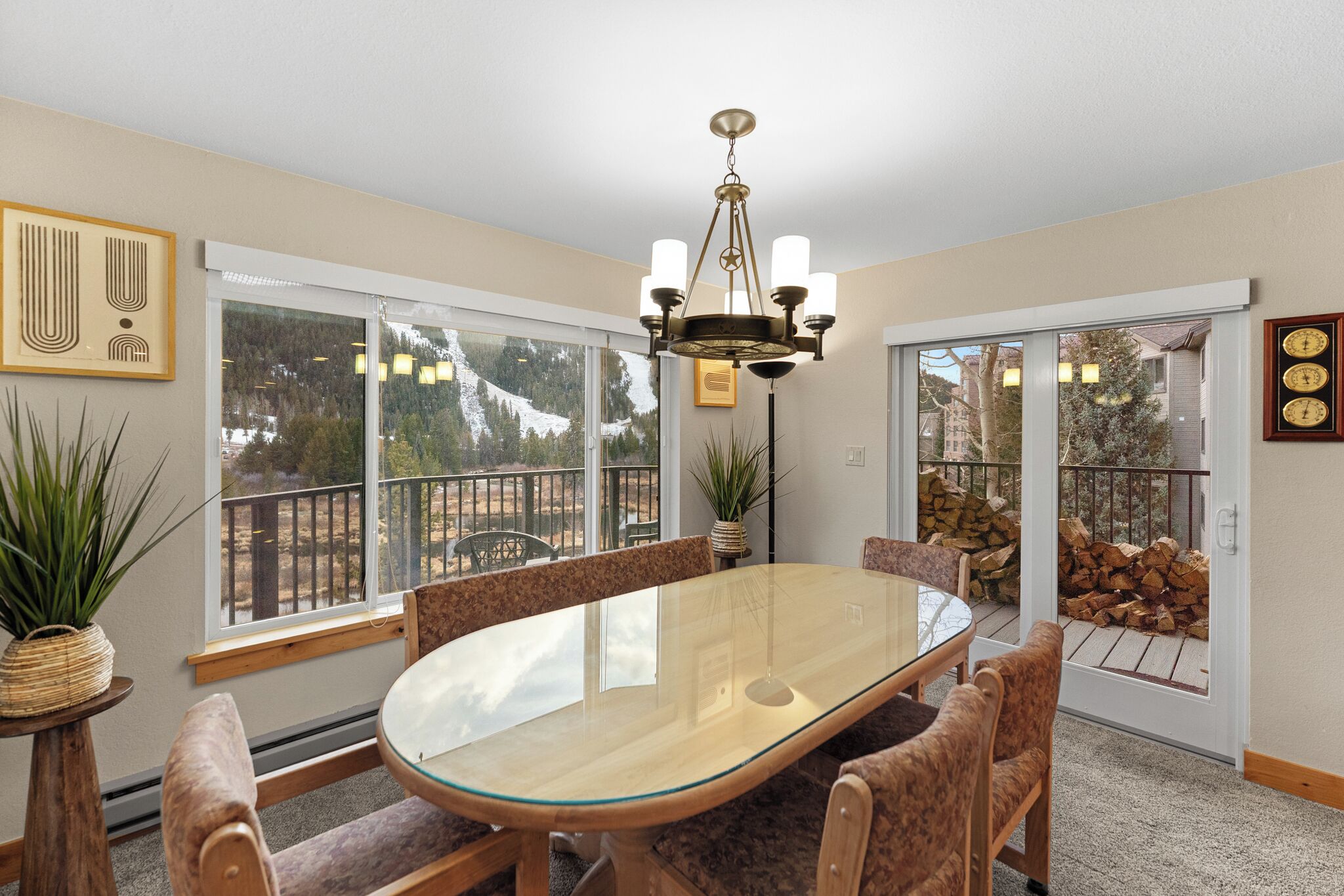 A dining area with a glass table, wooden chairs, a chandelier, and large windows offering a view of a snowy landscape.
