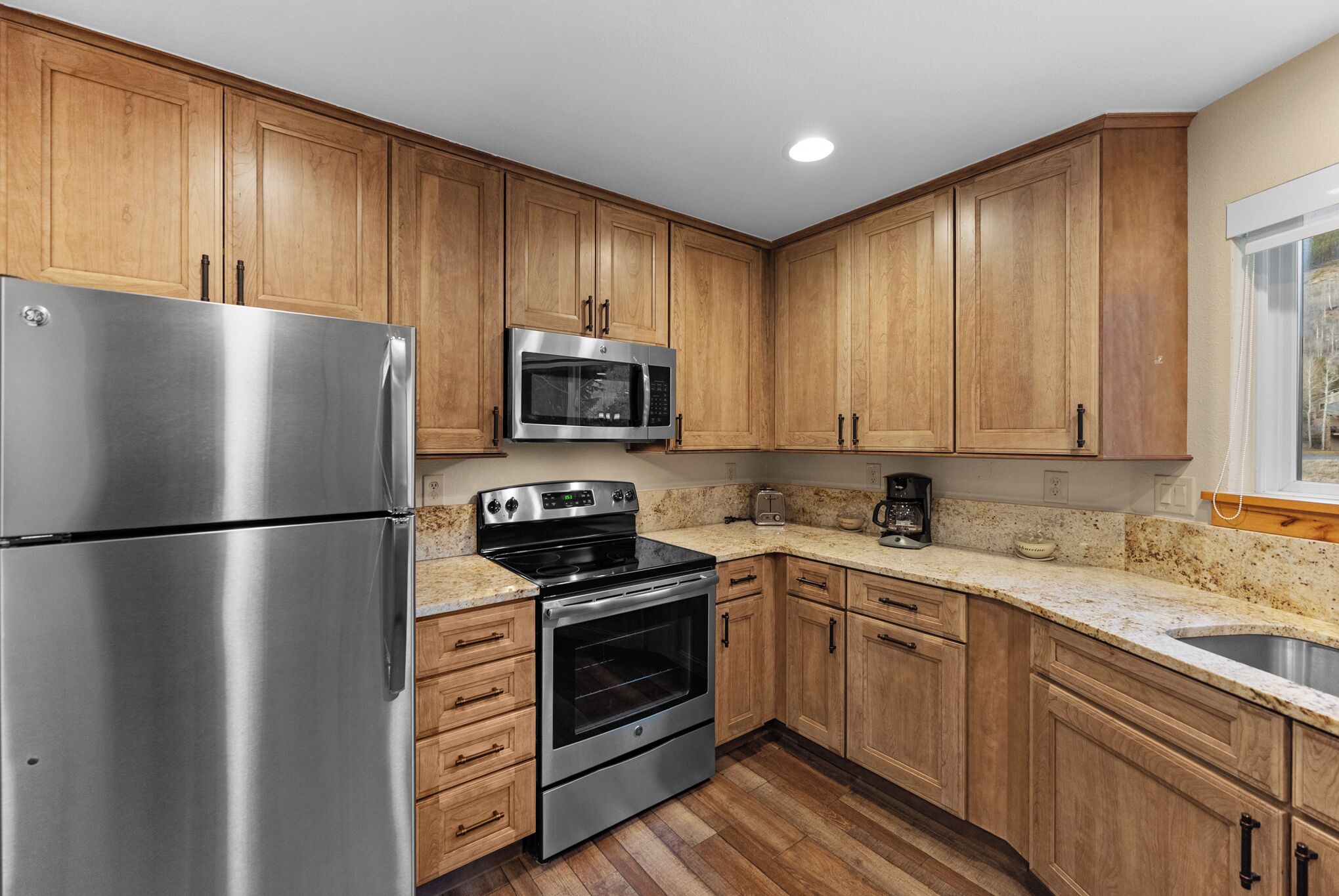 A modern kitchen with wooden cabinets, stainless steel appliances, and a granite countertop.