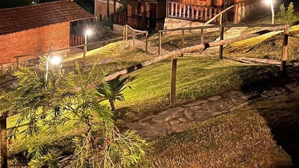 A rustic building with a wooden porch, surrounded by a well-lit garden and a clear night sky.