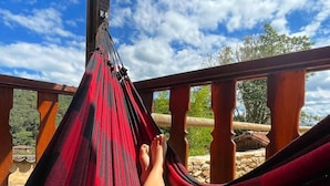A hammock tied between wooden posts on a balcony with a clear sky and greenery in the background.