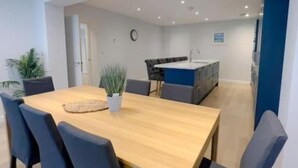 Un espace repas moderne avec une table en bois et six chaises, une petite plante et une cuisine en arrière-plan.