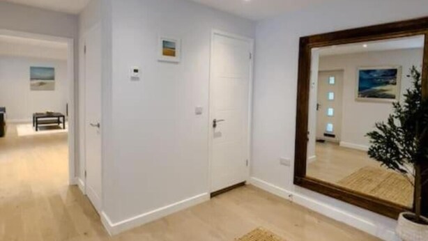 Une pièce spacieuse avec un grand miroir, un plancher en bois et une porte donnant sur une autre pièce.