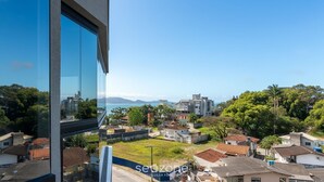 Un quartier résidentiel avec un immeuble moderne, un ciel bleu dégagé et une vue sur la mer au loin.