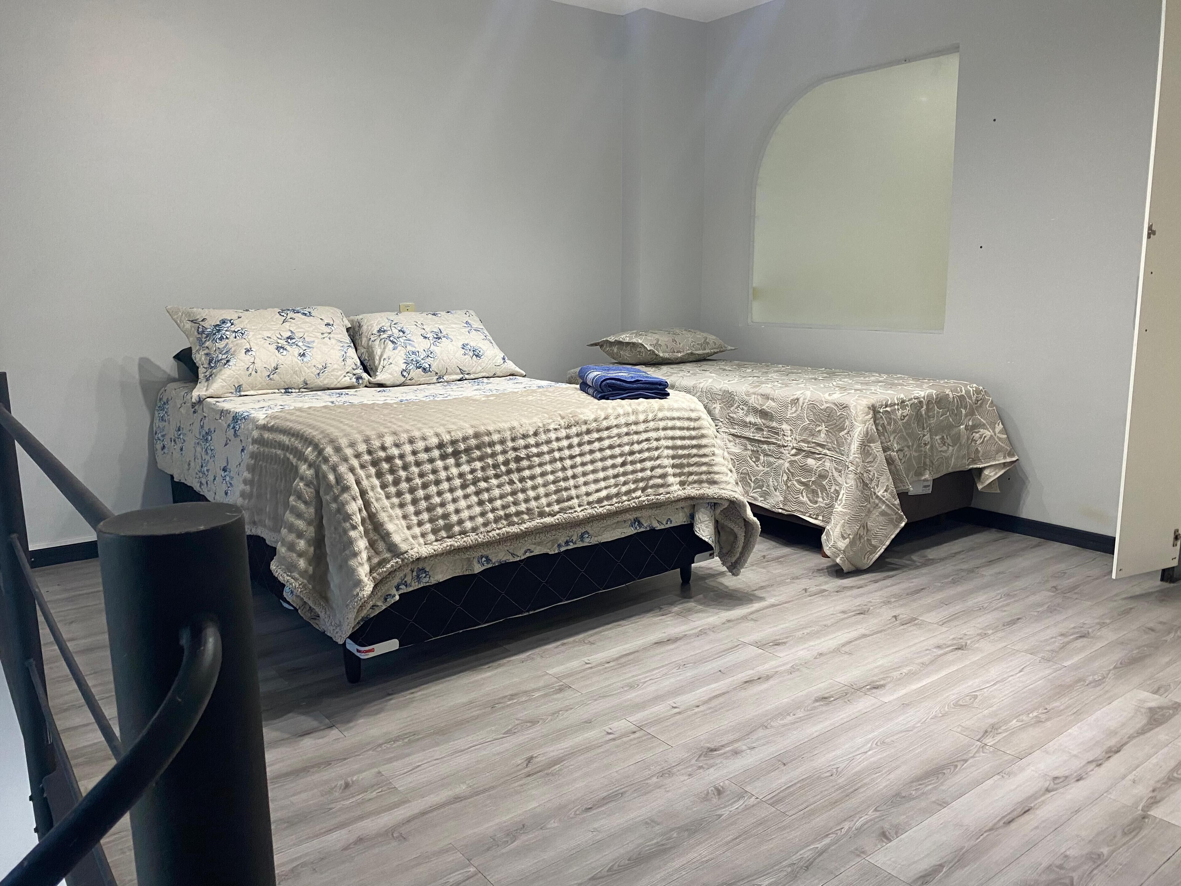 Un dormitorio con dos camas, piso de madera y un ventanal grande.