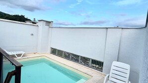 Un espace piscine aménagé sur le toit, offrant une vue dégagée sur le ciel, avec une piscine et des chaises longues blanches.