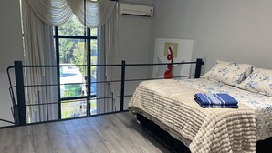 Une chambre à coucher comprenant un lit, des rideaux, un climatiseur, une fenêtre avec vue et une œuvre d’art accrochée au mur.