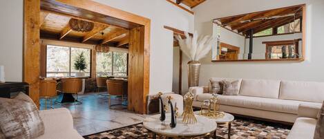 A spacious living area with a wooden ceiling, a sofa, a coffee table, and a dining area with chairs and a table.