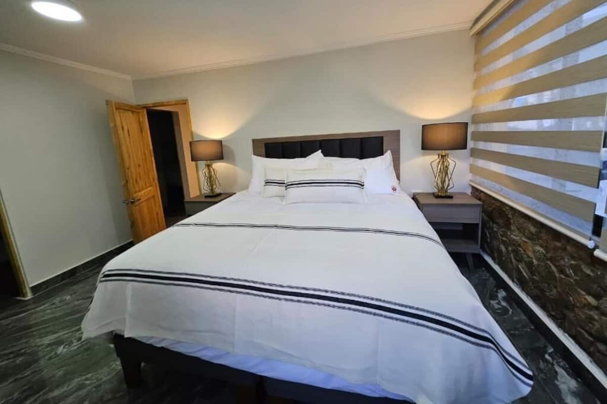 Hotelkamer met een groot bed, twee nachtkastjes met lampen, een houten deur en een gestreepte wand.