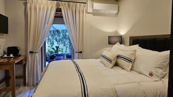 A bedroom with a bed, a desk, an air conditioner, and a view of trees.
