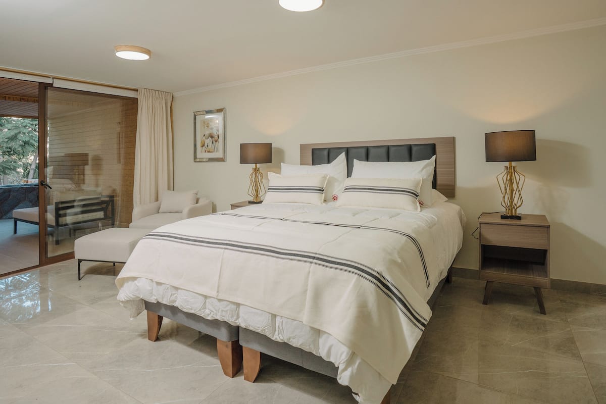 Een ruime slaapkamer met een groot bed, twee nachtkastjes met lampen, een schuifdeur naar een balkon, en een lijst met een afbeelding aan de wand.