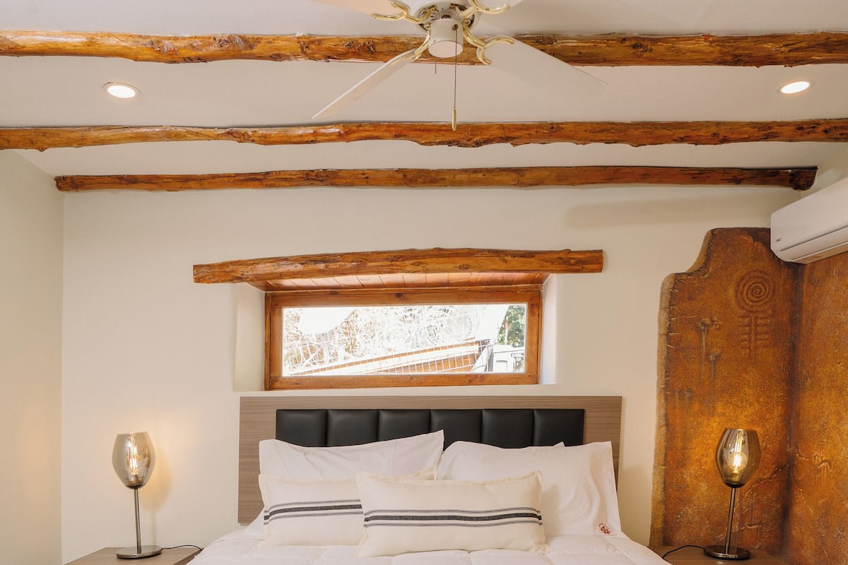 Een slaapkamer met een groot bed, houten balken, een plafondventilator en een raam met uitzicht.