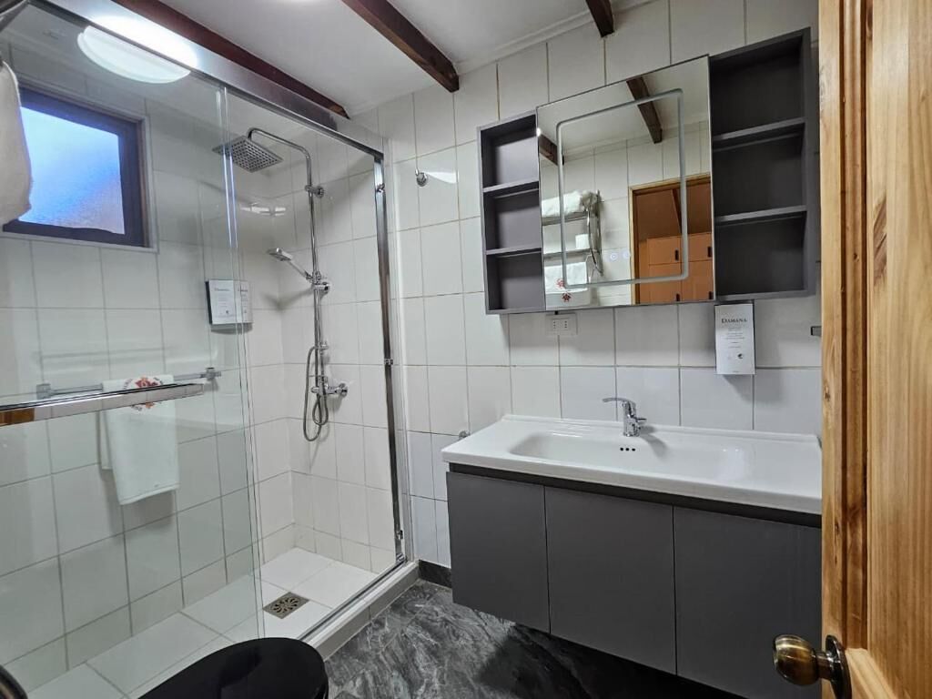 A bathroom with a glass-enclosed shower, a sink with a mirror above it, and a wooden door.