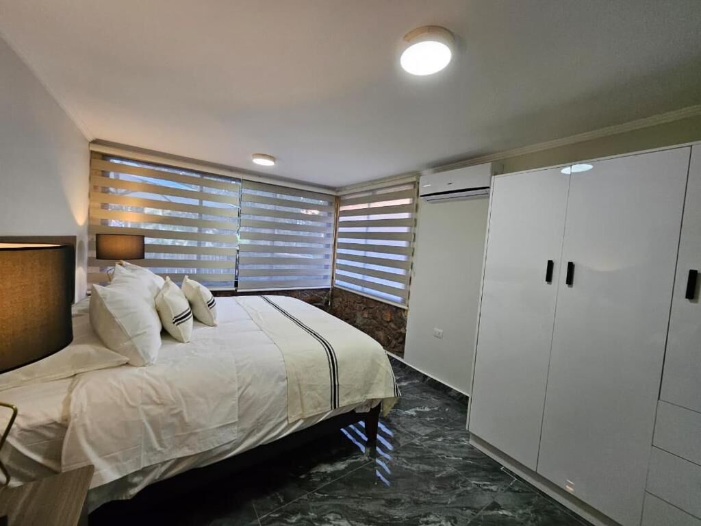 Un dormitorio con cama, mesita de noche, televisor montado en la pared y armario.