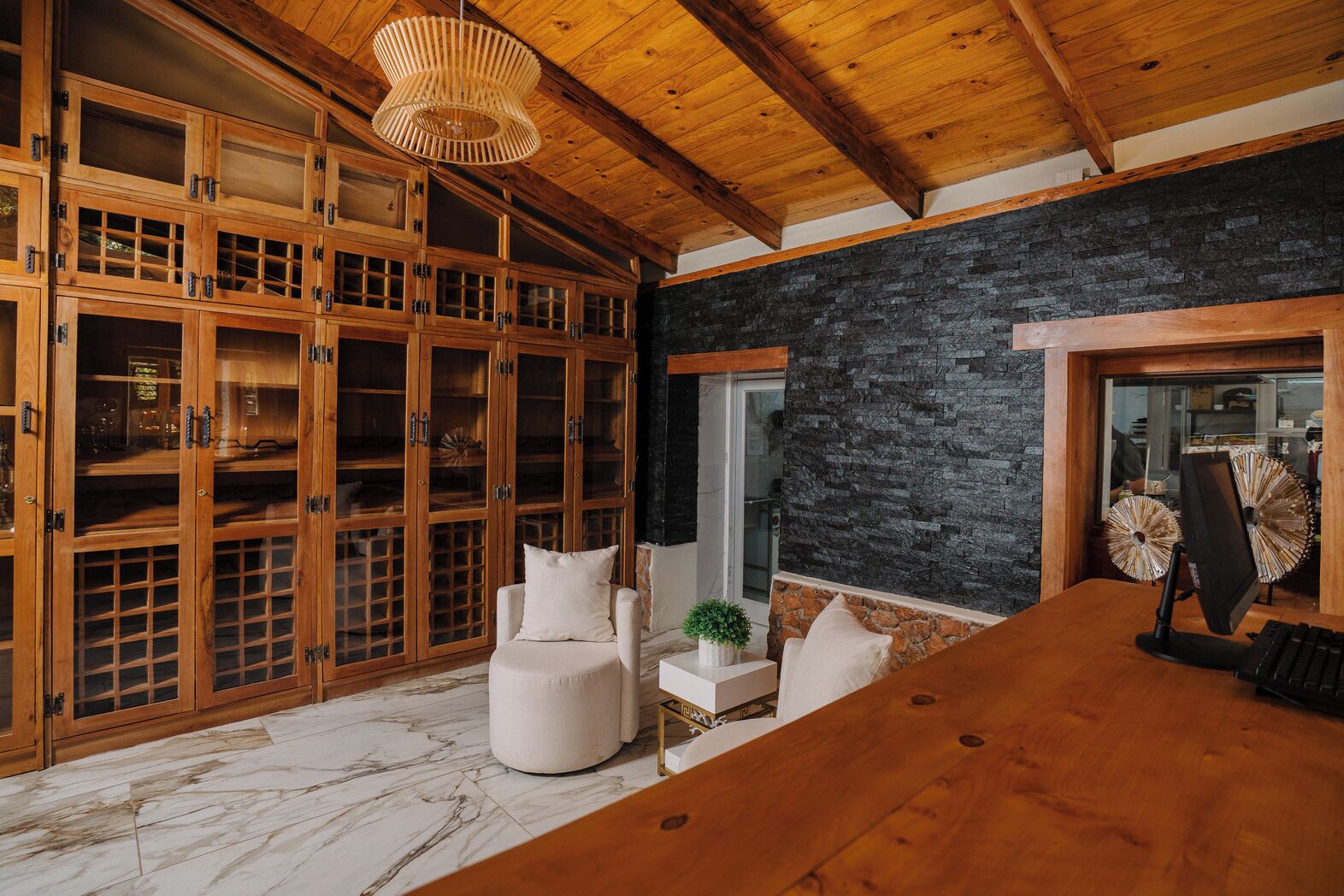 Una habitación amplia con techo de madera, pared de piedra y un mueble grande de madera con puertas de cristal.
