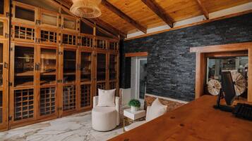 Una habitación amplia con techo de madera, pared de piedra y un mueble grande de madera con puertas de cristal.