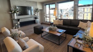 Ein modernes Wohnzimmer mit Flachbildfernseher, bequemen Sitzgelegenheiten, einem Kamin und großen Fenstern mit Blick auf die Stadt.