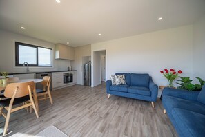 Eine moderne Küche mit Holzschränken, ein Essbereich mit Tisch und Stühlen, ein blaues Sofa und ein kleiner Beistelltisch mit Blumen.
