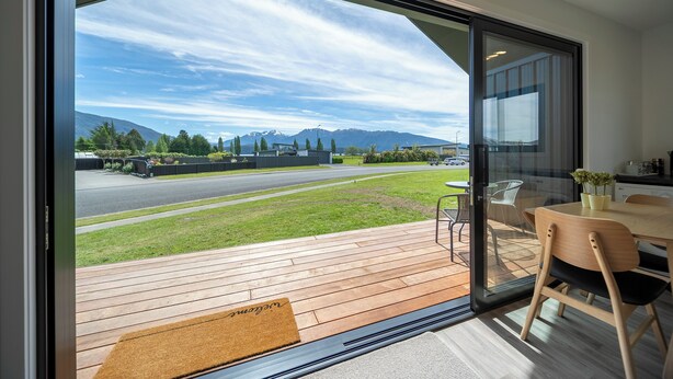 Un interno moderno con una porta scorrevole in vetro che dà su un patio, un tavolo di legno e una sedia.