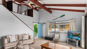 Una sala de estar con sofá, una mesa de centro, un televisor sobre un mueble bajo y una ventana con cortinas.