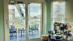 A room with a sliding glass door leading to an outdoor deck with a table and chairs. - Saltwater Solace, For 8 (Galveston)