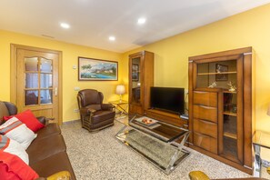 Een woonkamer met een bruine leren bank, een glazen salontafel, een televisie, een houten kast en een schilderij aan de muur.