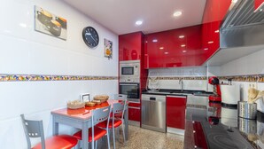 Una cocina moderna con armarios rojos, microondas, horno y lavavajillas. Cuenta con una mesa de comedor con sillas y un reloj en la pared.
