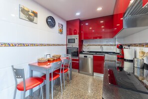 Uma cozinha moderna com armários vermelhos, micro-ondas, forno e lava-louças. Há uma mesa de jantar com cadeiras e um relógio na parede.