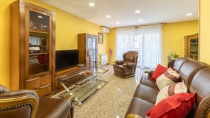 Una sala de estar con un sofá, sillones, una mesa de centro de vidrio, un televisor y un aparador.