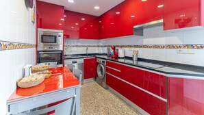Una cocina moderna con armarios rojos, electrodomésticos de acero inoxidable y un salpicadero de azulejos.