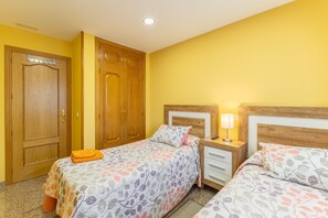 Een kamer met twee bedden, houten kasten, een nachtkastje met een lamp en een vloerbedekking.