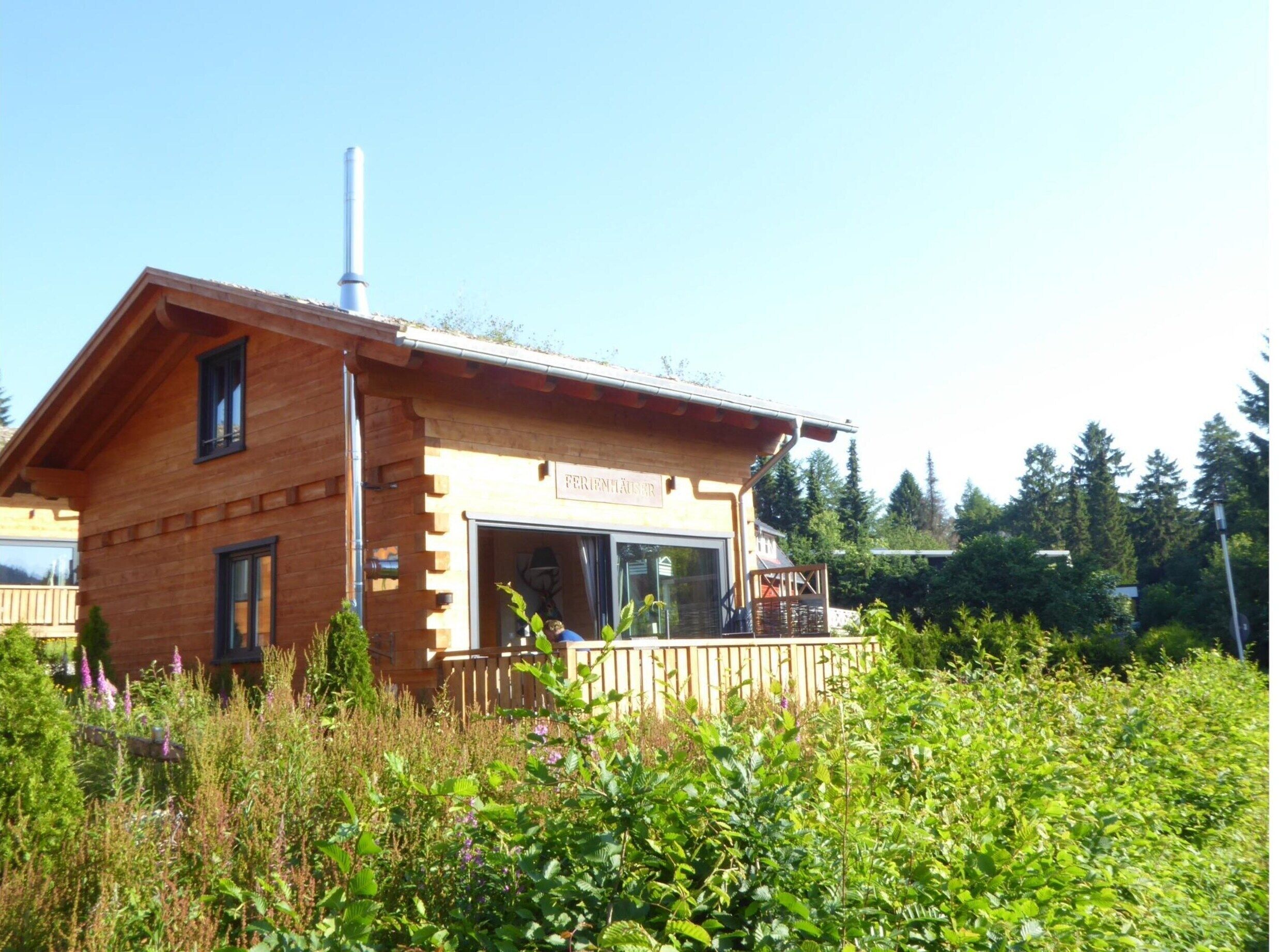 Un chalet en bois avec une cheminée, une enseigne indiquant « FERIENHAUS », et une terrasse en bois.