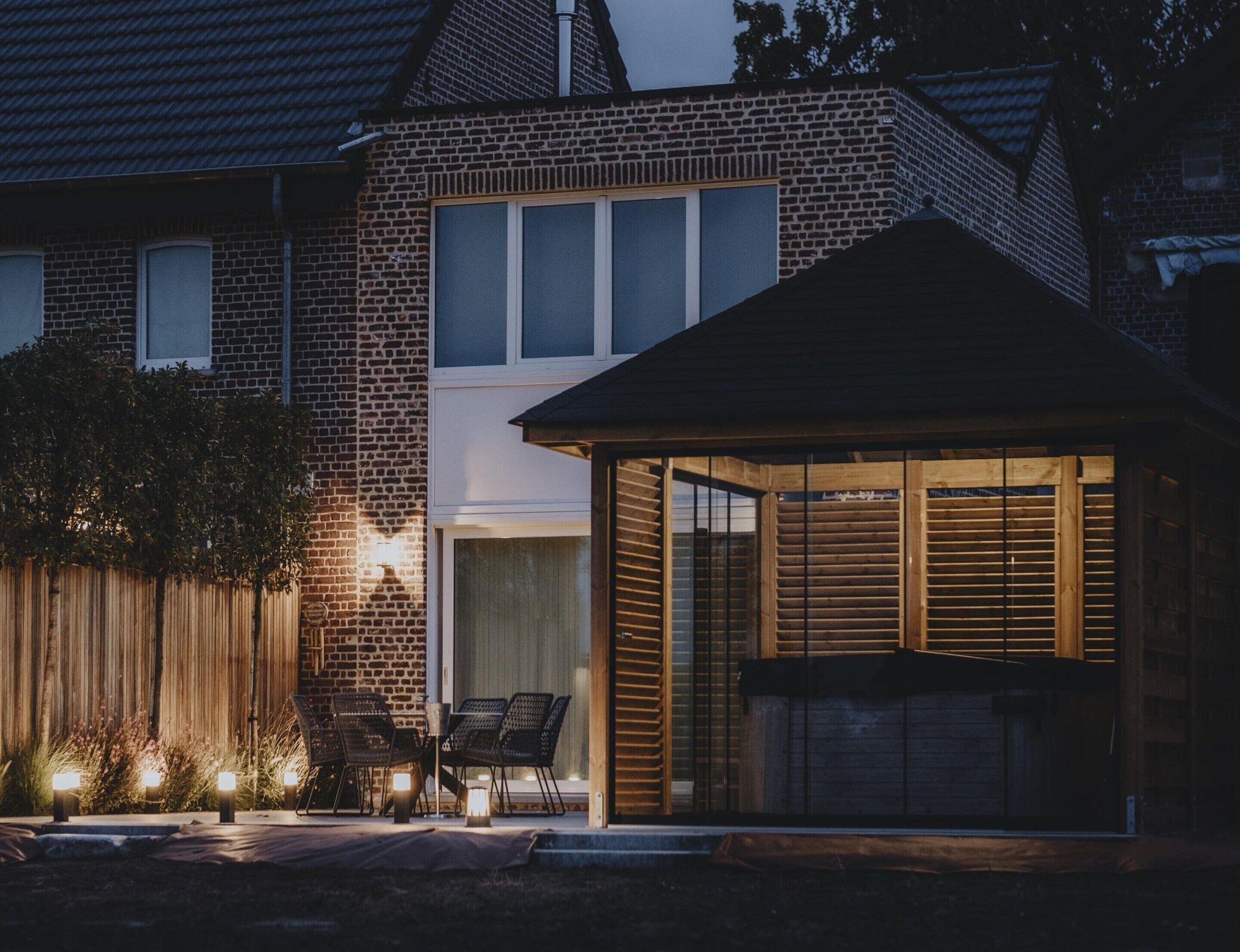 A brick house with a covered patio area, outdoor seating, and a wooden structure with shutters.