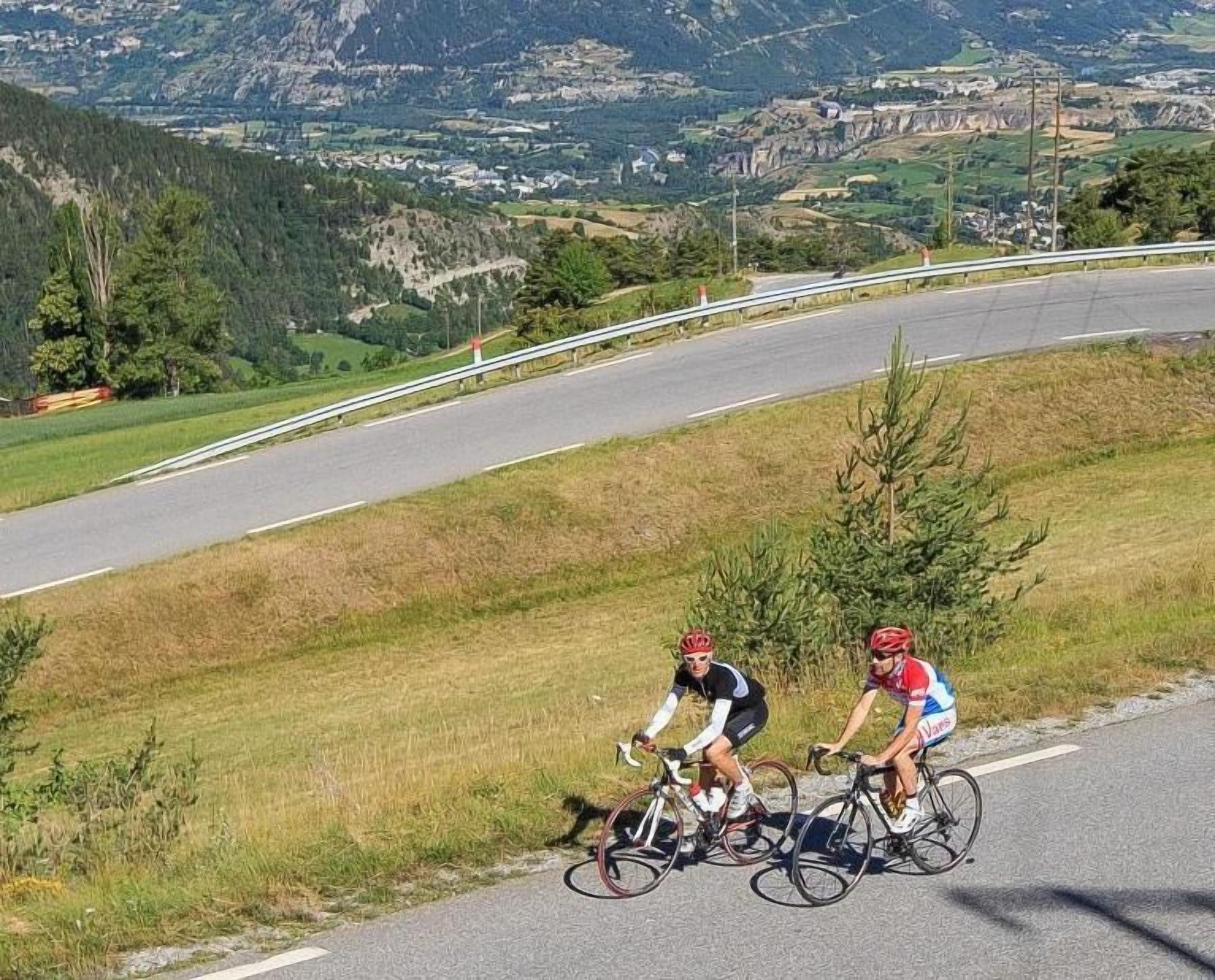 Two cyclists on a road with a mountainous landscape in the background.