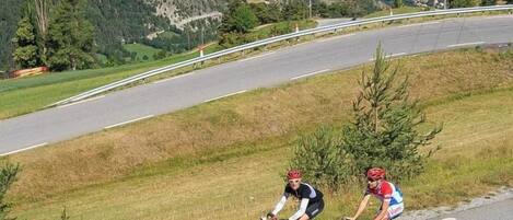 Two cyclists on a road with a mountainous landscape in the background.