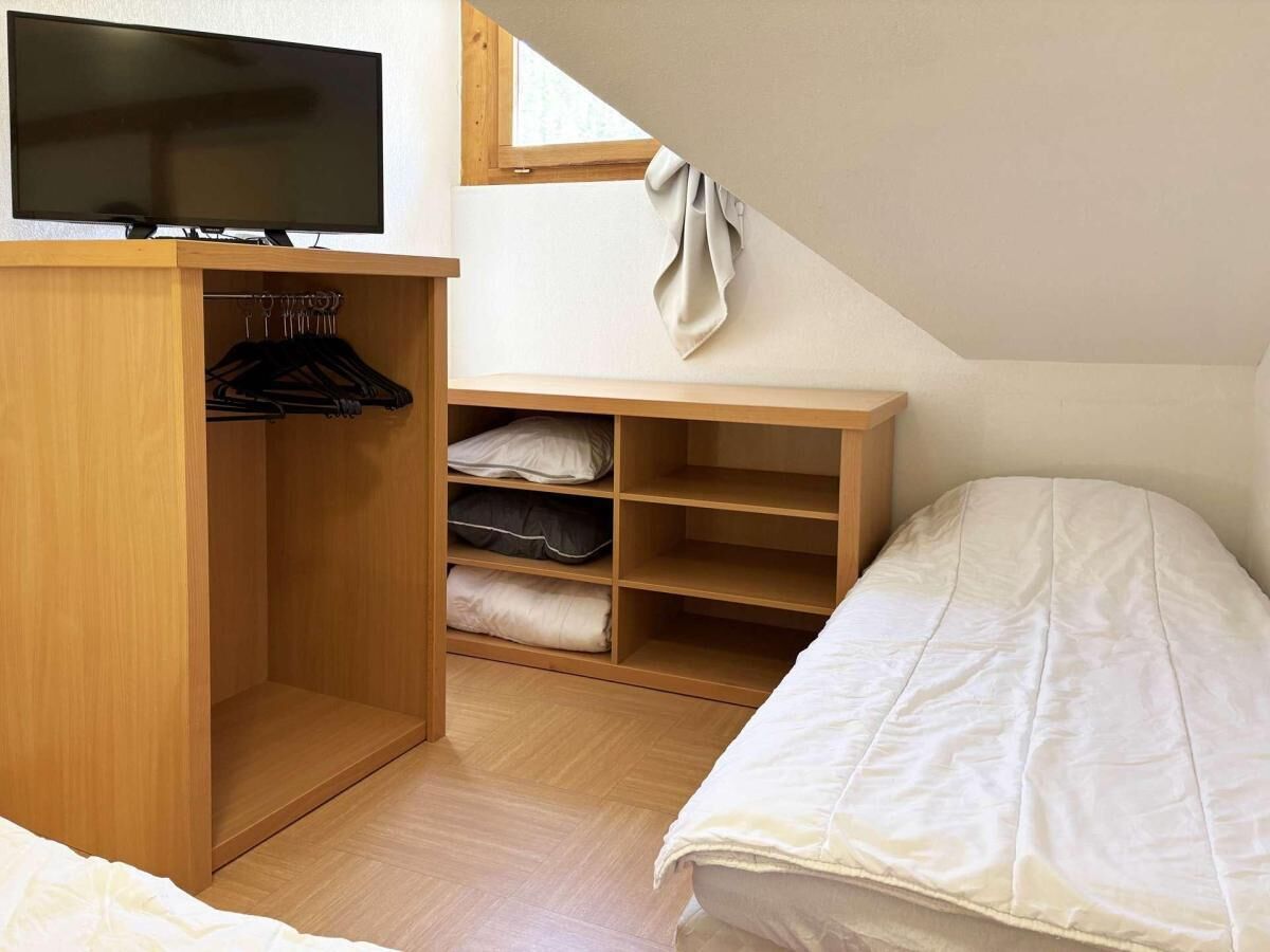 Ein Schlafzimmer mit einem Bett, einem Fernseher, einem Holzschrank und einem Fenster.