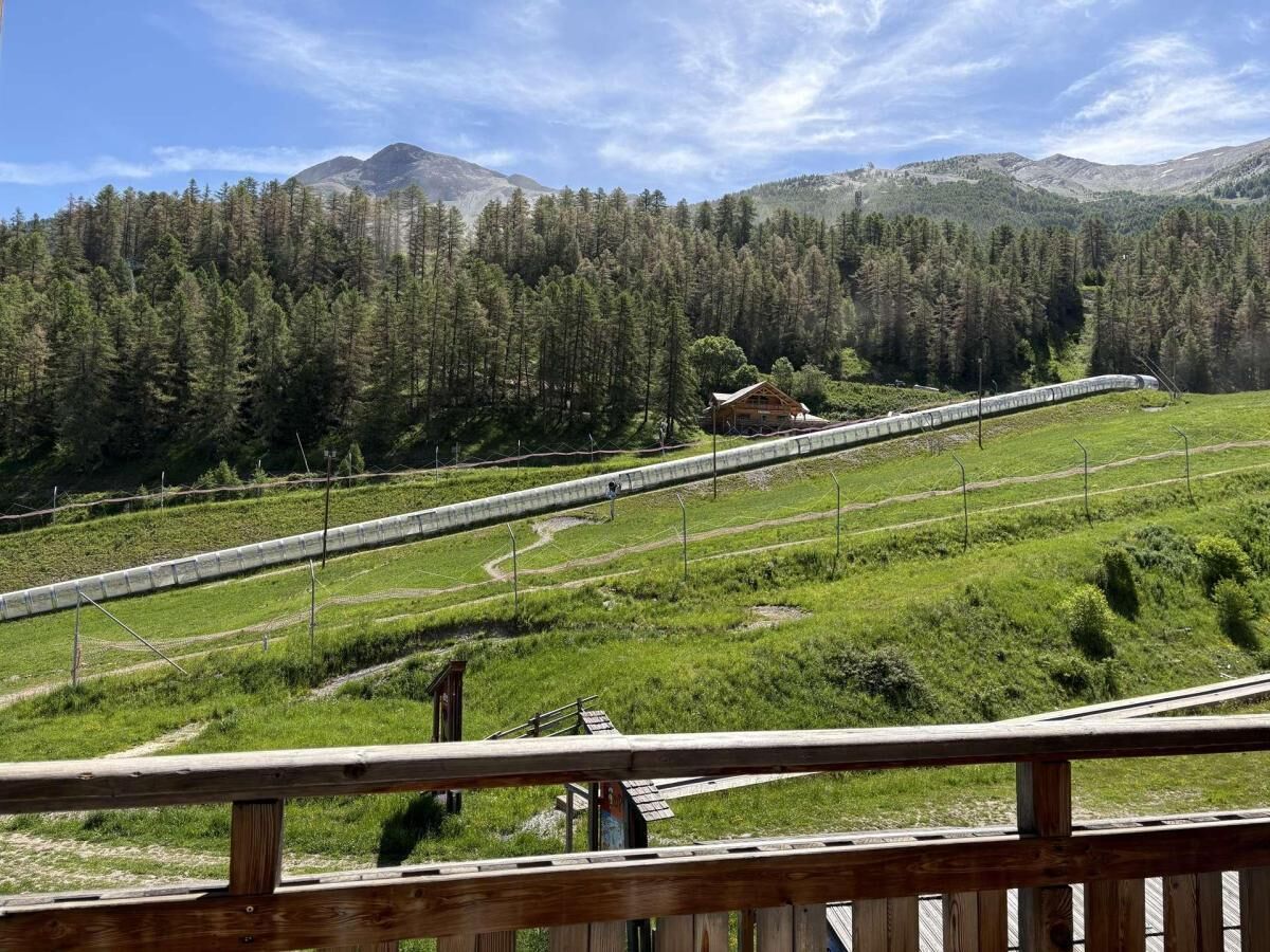 Una terraza de madera con vistas a un paisaje montañoso, una cabaña de madera y un puente largo y estrecho.