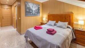 A hotel room with a wooden paneled wall, a large bed with a grey quilt, two bedside tables with lamps, and a framed cityscape picture on the wall. - Penthouse 'Pensado Para Ti' in Pozuelo de Alarcón - Central Madrid Area (Pozuelo de Alarcón)