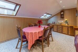 Un comedor con una mesa dispuesta para seis personas, sillas de madera, mantel rojo y una planta en maceta.