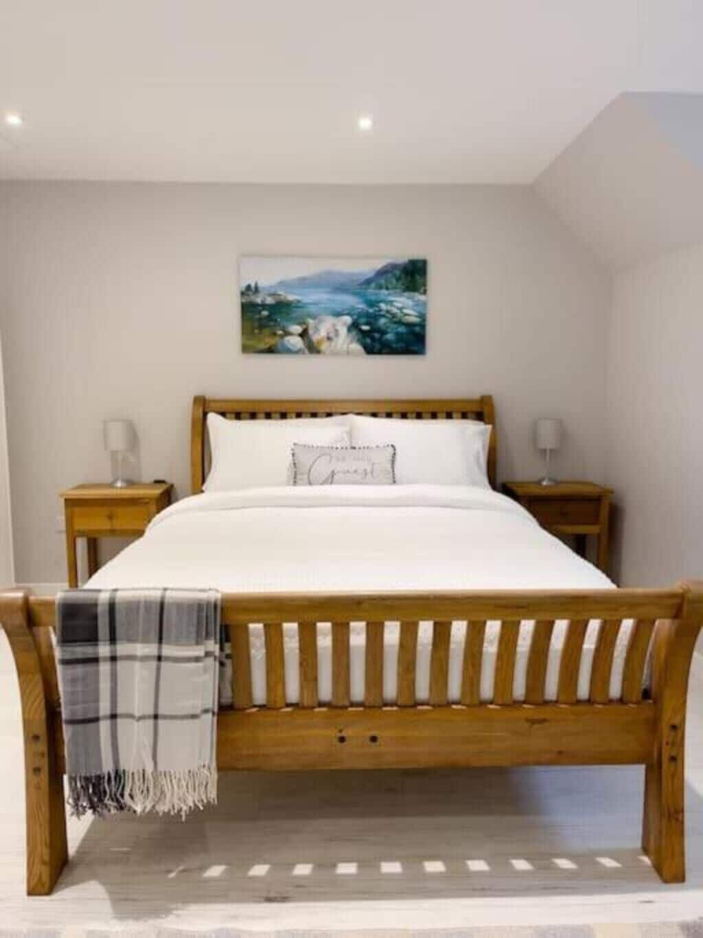 Ein Schlafzimmer mit einem Holzbettgestell, weißer Bettwäsche und einem Landschaftsbild an der Wand.